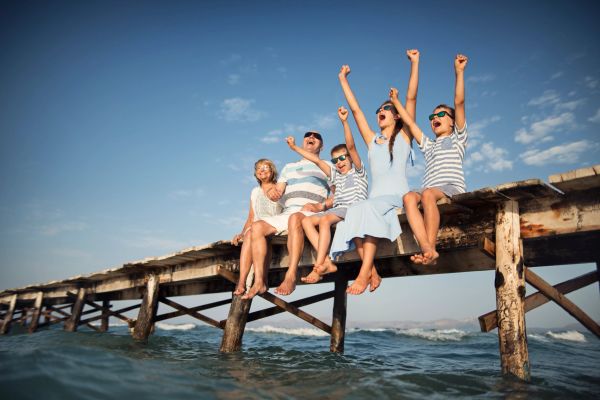 Family enjoying sunny day sitting on pier above water.