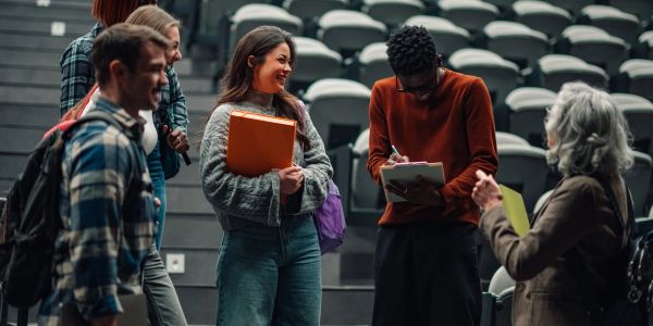 Students chatting and signing papers in an auditorium.