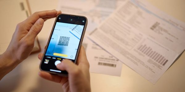Persona escanea código QR en teléfono móvil frente a documentos.