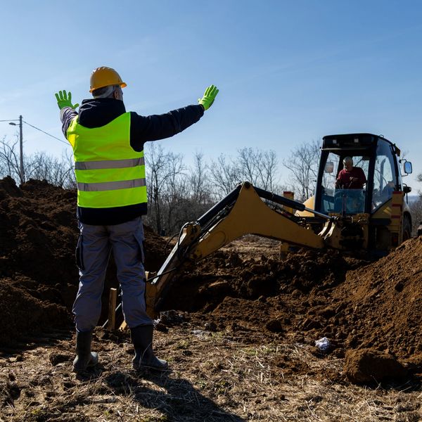 Construction worker directing excavator at a digging site.