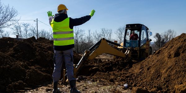 Construction worker directing excavator at a digging site.