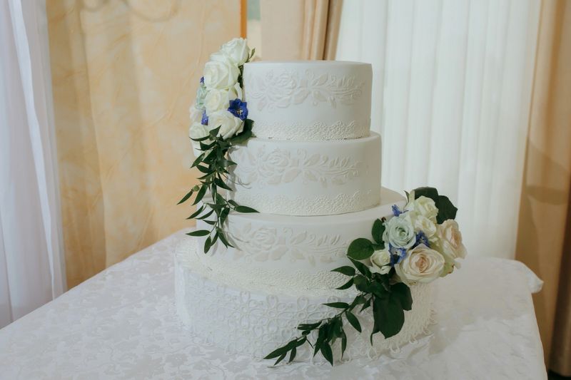 A white three tier wedding cake with blue flowers and white flowers on it. The cake is decorated with a blue ribbon and a white ribbon