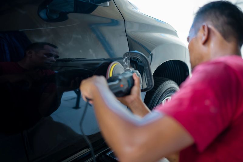A professional auto detailer uses an electric polishing machine to buff and polish the surface of a car door. The image captures the car detailing process, highlighting vehicle maintenance, surface polishing, and professional automotive care. Professional car detailer and rotary polisher machine