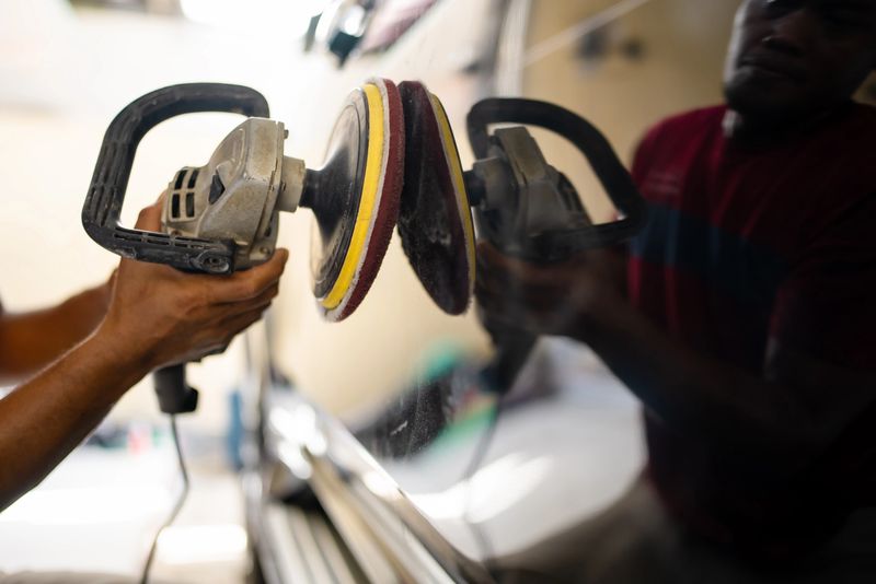 A professional auto detailer uses an electric polishing machine to buff and polish the surface of a car door. The image captures the car detailing process, highlighting vehicle maintenance, surface polishing, and professional automotive care. Professional car detailer and rotary polisher machine