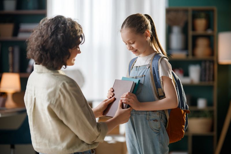 Heartwarming interaction between a caring teacher and a cheerful young student, illustrating the joy of learning and support in education. The cozy, modern classroom interior emphasizes a nurturing, inspirational atmosphere perfect for academic achievement and personal growth. Ideal image for concepts of mentorship, encouragement, childhood development, and positive school experiences.