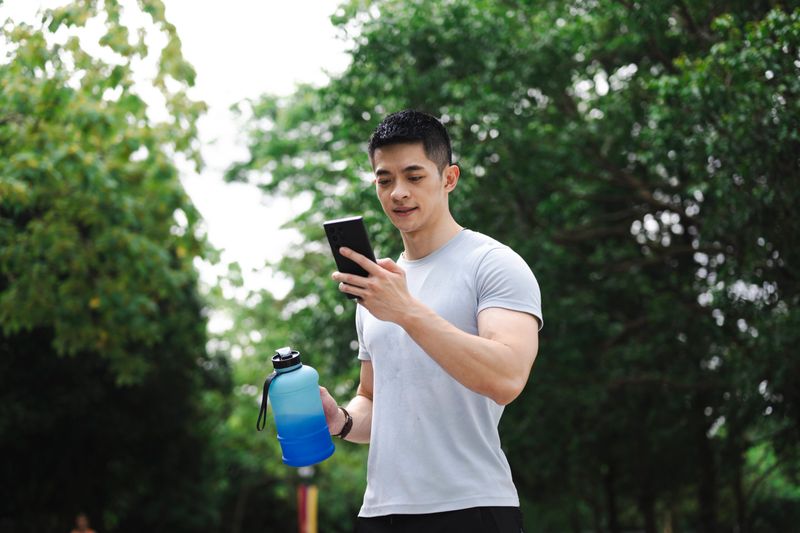 A man drinks water after exercise and looks at his phone, highlighting a modern and active lifestyle.