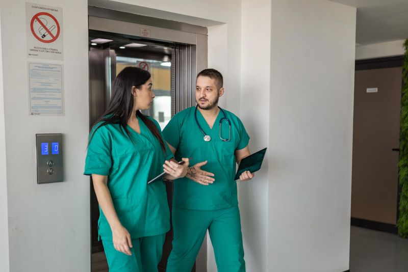 Medical team collaborating and communicating while walking past elevator in modern hospital