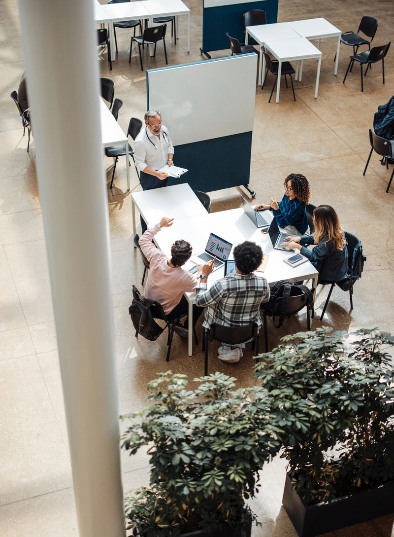 A close-up view of students actively participating in an interactive learning session in a bright and cozy workspace, supported by their instructor, surrounded by greenery.