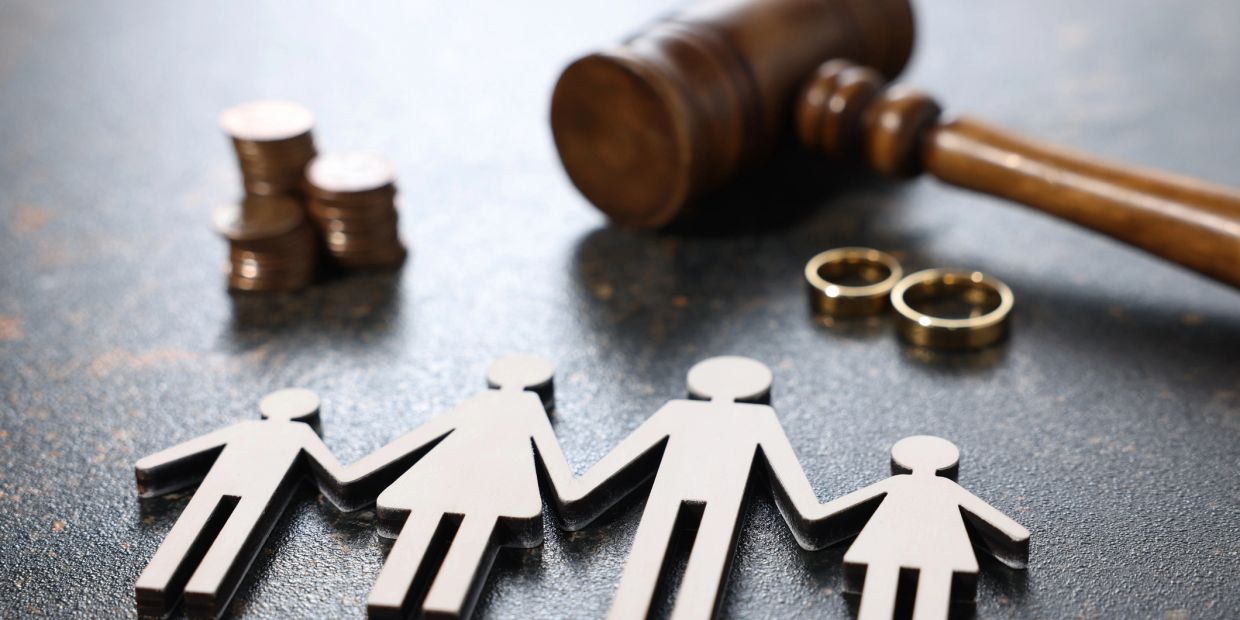 Wooden family cutouts, wedding rings, gavel, and coins representing legal and financial family matters.