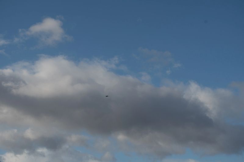 A small drone flies against a dynamic blue sky filled with a mix of bright white and dark grey clouds, creating an atmospheric outdoor scene.