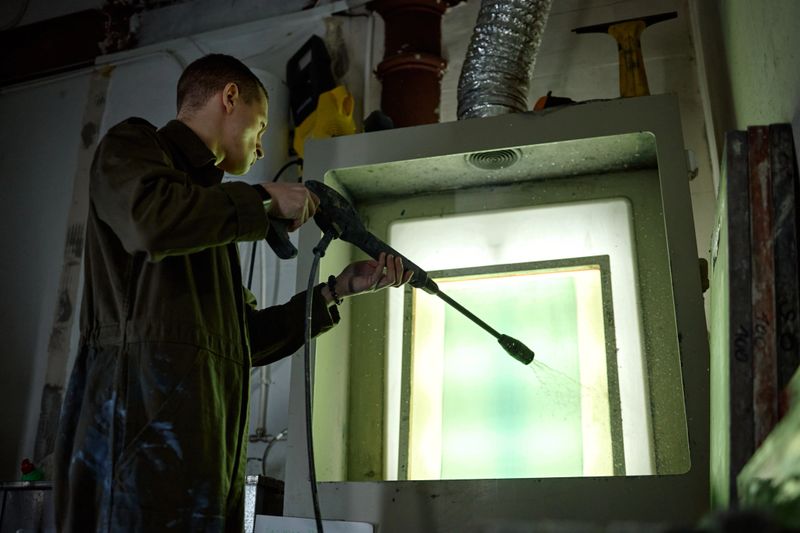 Young adult Caucasian man cleaning industrial equipment with high pressure washer inside workshop, standing in front of large metal enclosure, focusing on maintenance task