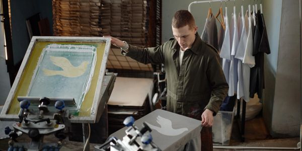 A man screen printing a bird design on fabric.