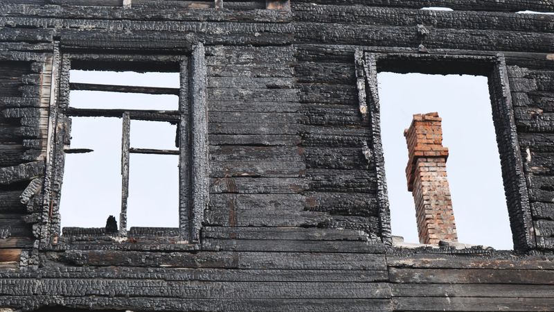 Destroyed wooden house wall after a fire, displaying dark charcoal texture and an exposed chimney