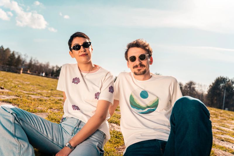 Sustainable lifestyle and eco-conscious living. A young couple is relaxing outdoors in sunlight wearing eco-friendly clothing and sunglasses promoting green fashion and ethical consumerism in a park.