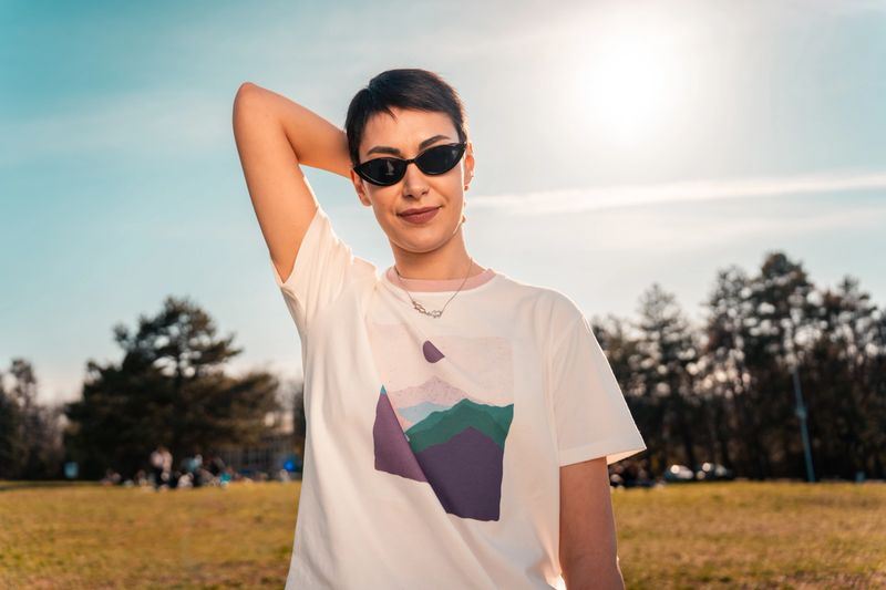 Sustainable lifestyle and eco-consciousness. A woman stands in a park wearing a t-shirt with a mountain design representing environmental awareness and a connection to nature.