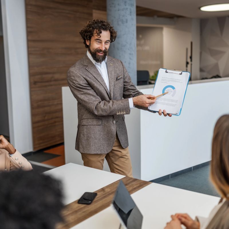 Businessman presenting financial data using a chart and pointer to colleagues during a professional corporate meeting