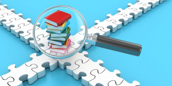 Magnifying glass over stack of books on puzzle pieces.
