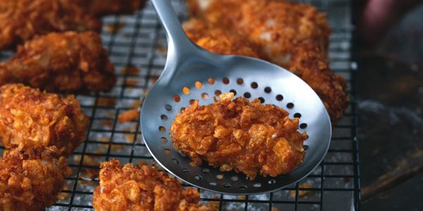 Golden crispy fried chicken resting on a perforated metal spoon.