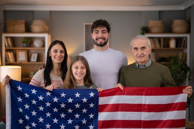 A diverse family holding an American flag indoors, smiling.