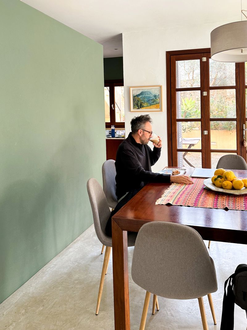 Authentic lifestyle scene of a man sitting at the dining table in his home, calmly having breakfast on a bright sunny morning. Natural light fills the room, capturing a quiet everyday moment from a day in the life, representing home routine, relaxation, and a simple morning lifestyle. Ideal for concepts such as daily life, morning routine, healthy living, home lifestyle, remote life, and peaceful moments.