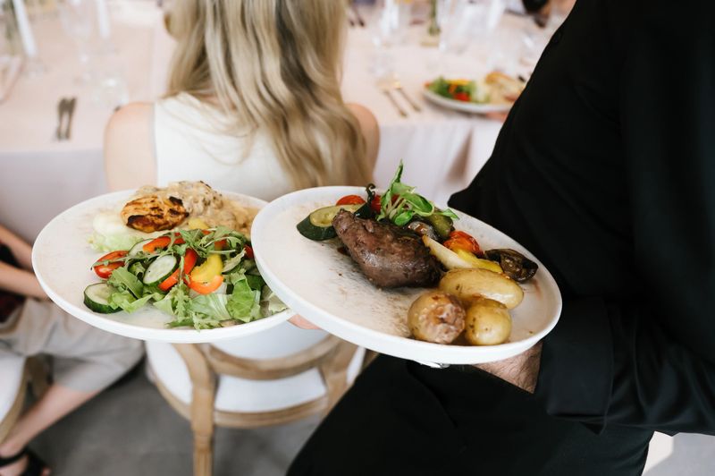Waiter carrying plated meals during wedding reception service, showcasing professional hospitality and elegant dining experience in celebration setting