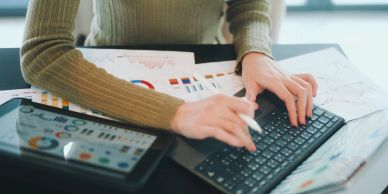 Person working on laptop with tablet and charts.