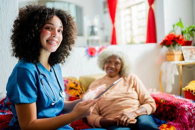 Nurse smiling while attending to an elderly woman at home.