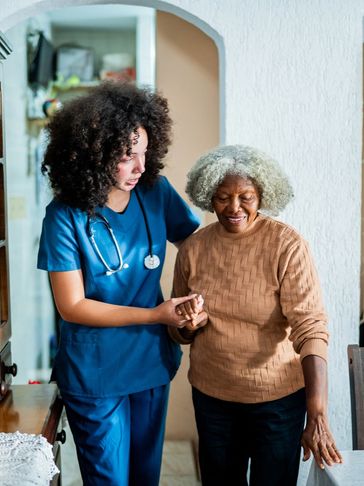 Nurse assists elderly woman walking indoors.