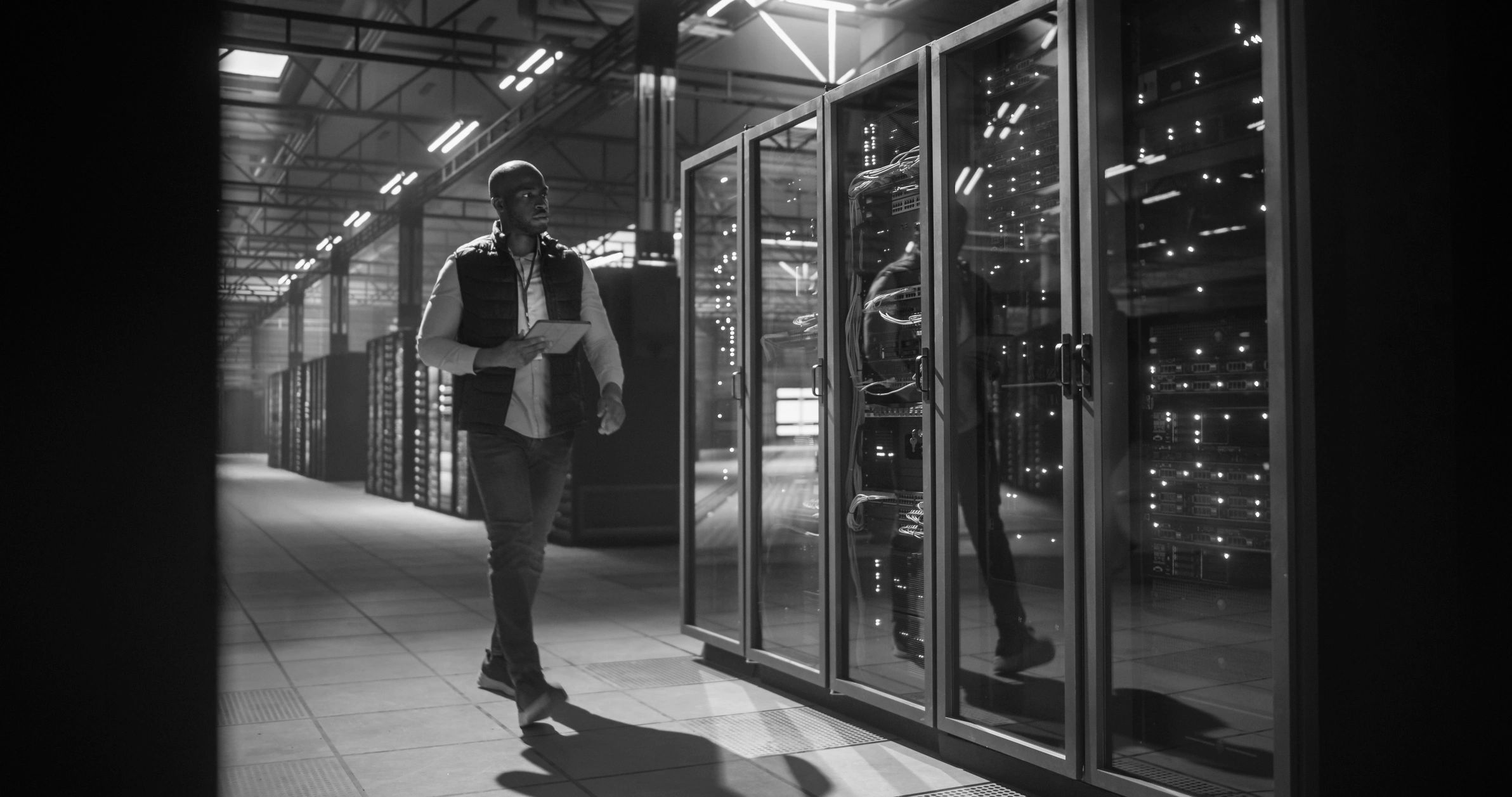 An engineer walking a data centre aisle, reviewing a running system rather than a document