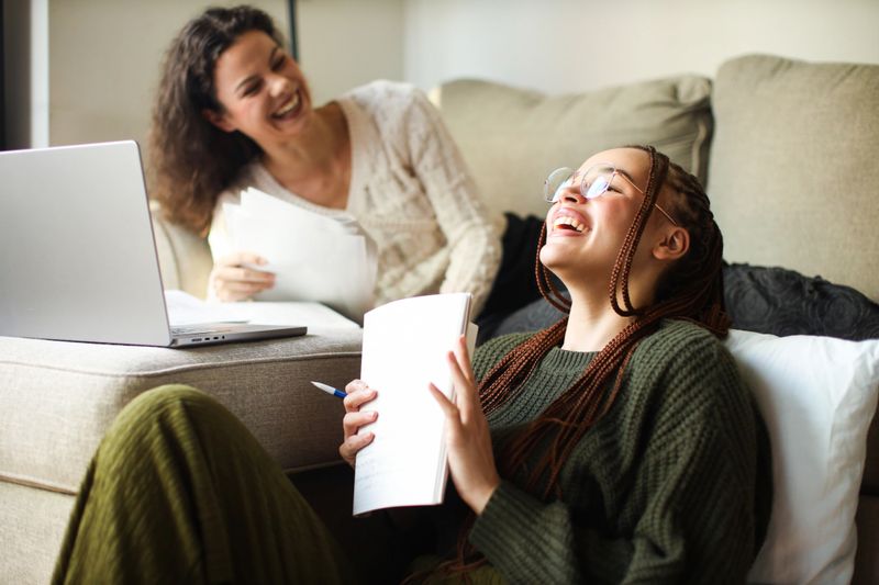 Young women engaged in academic research, surrounded by study materials, working together in a modern urban apartment in New York.