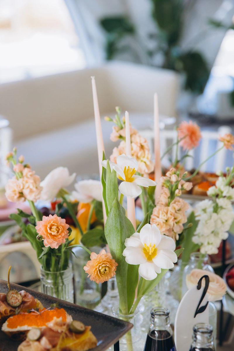 Elegant wedding reception table presenting a beautiful floral centerpiece with various fresh blooming flowers, taper candles, and small appetizers