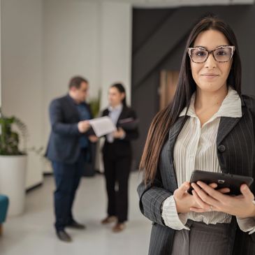 Confident businesswoman with tablet in focus, two colleagues discussing in background.