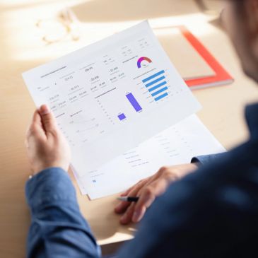 Person reviewing financial charts and data on paper at a desk.
