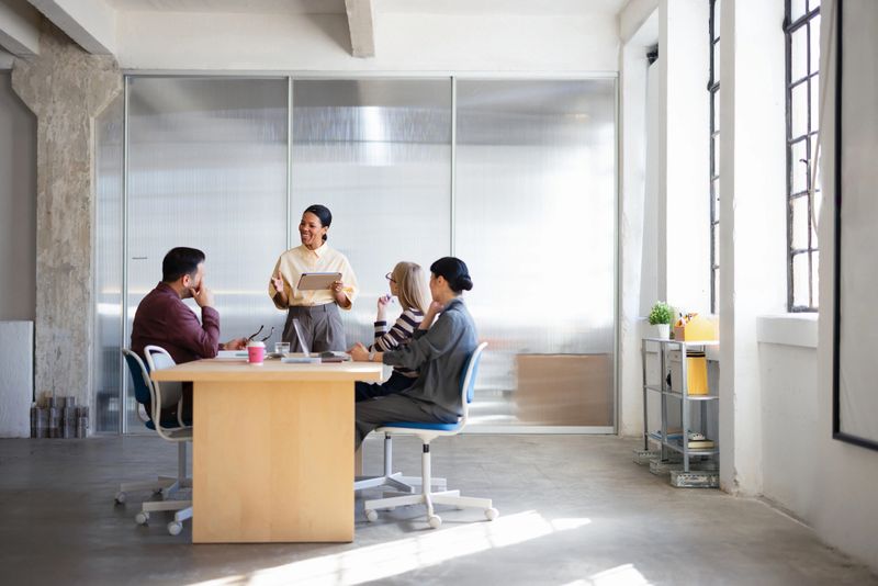 Colleagues discuss ideas as a presenter leads a collaborative business meeting in a bright office.