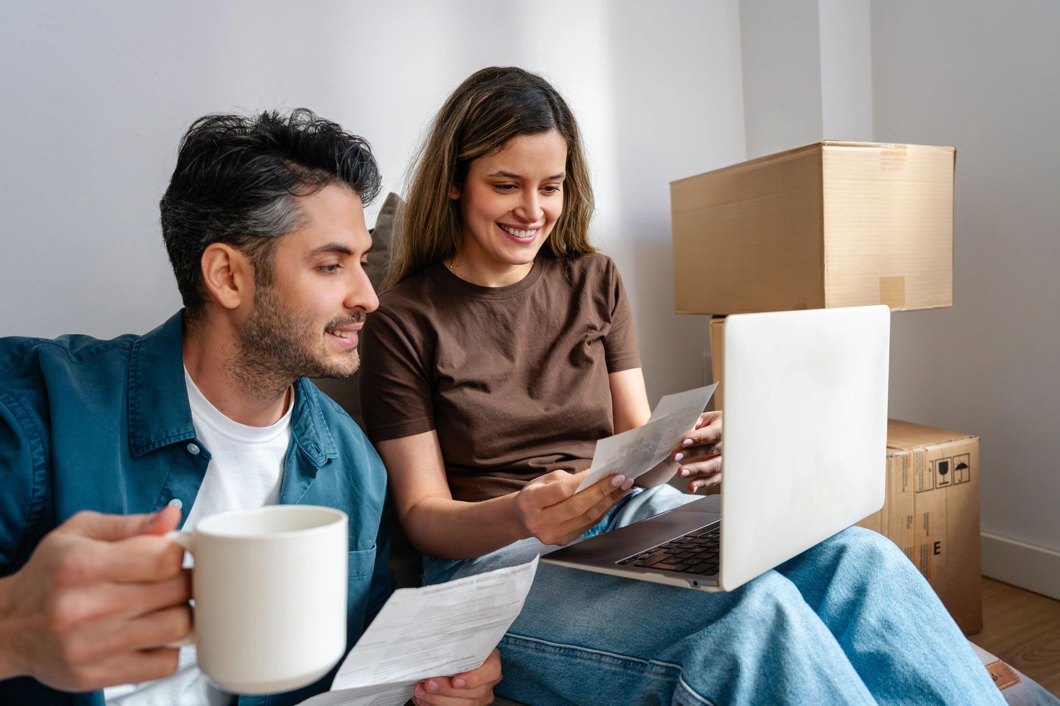 Couple reviewing documents and laptop with moving boxes nearby.
