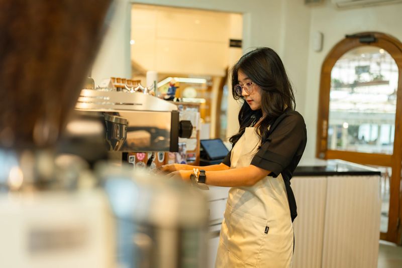 A barista focused on preparing coffee behind the counter in a cozy café setting. The scene captures the everyday workflow of a coffee shop, highlighting coffee culture, beverage preparation, and the atmosphere of a modern café environment.