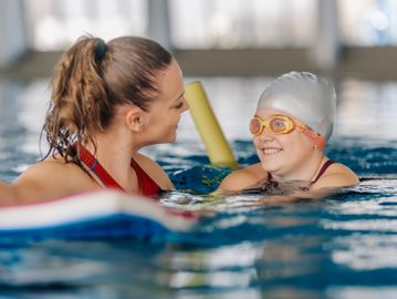 A swimming instructor smiles at a child in a pool during a lesson.
