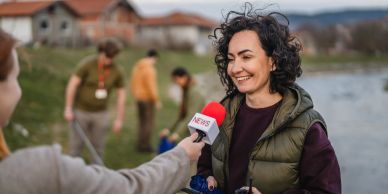A woman being interviewed outdoors near a lake.