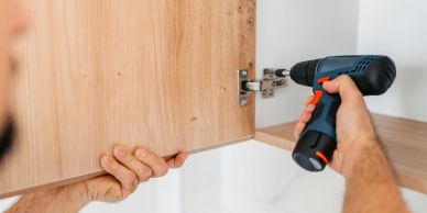 Person installing a cabinet door using a power drill.