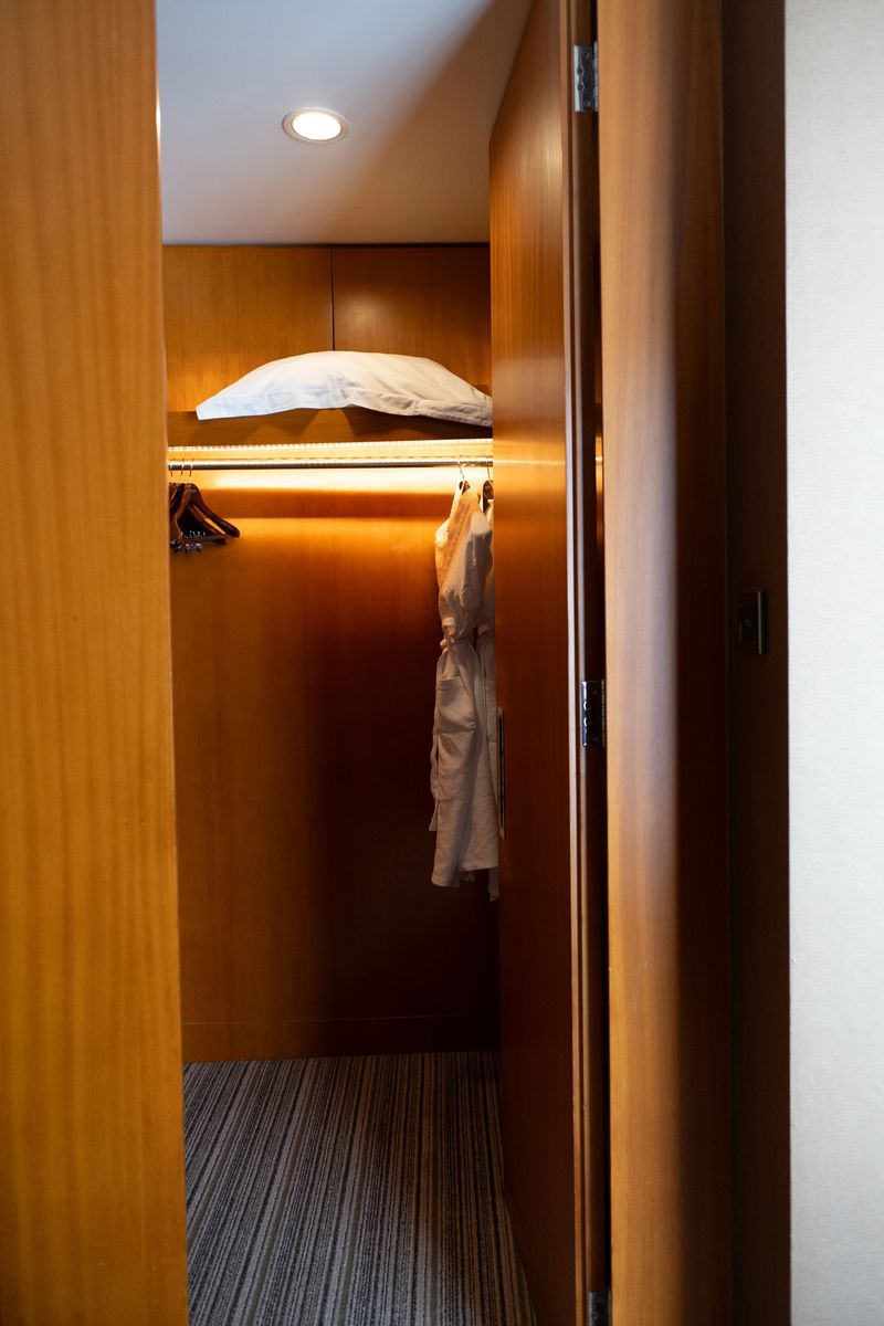 Modern hotel walk-in closet with wooden panels, hanging robe, and illuminated shelf in New York City
