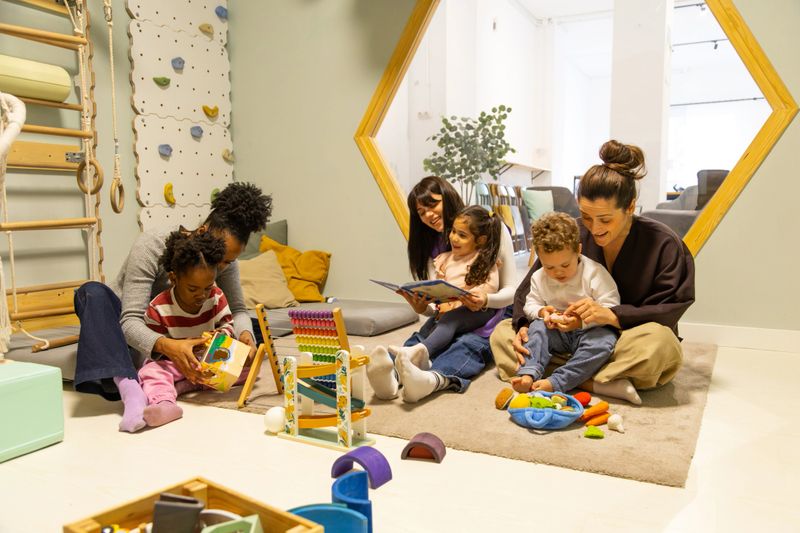 Adult teachers interacting with young children in a daycare classroom, reading books and playing with educational toys