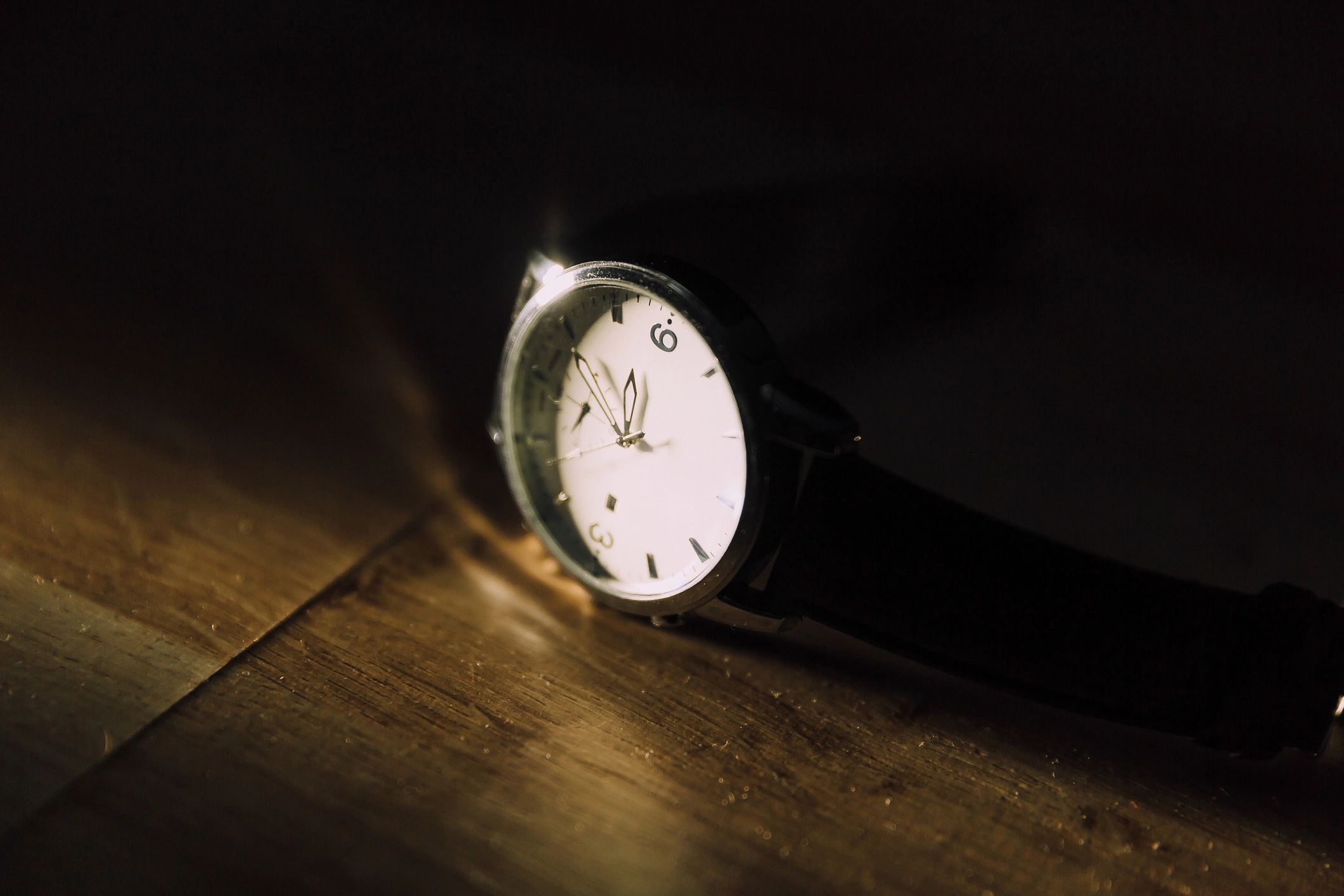 Close-up of a watch on a wooden surface in dim light.