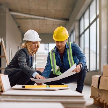 Two construction professionals reviewing blueprints at a building site.