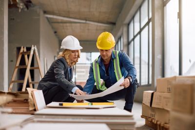 Two construction workers reviewing blueprints inside a building.