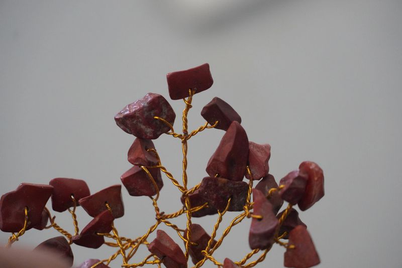 A close-up shot of a unique decorative tree made from golden wire and chunky, dark red garnet gemstones. This item embodies elegance and a touch of mystical charm.