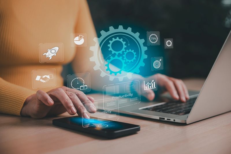 Businesswoman optimizing workflow with digital automation tools on smartphone and laptop. Concept of productivity, artificial intelligence, and strategic management in a modern office setting.