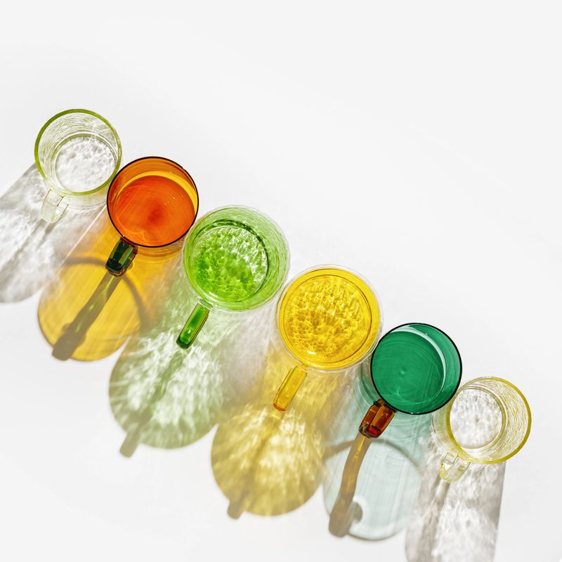 Set colored glass cups from transparent and clear glasses with beautiful shadow at sunlight, summer drink for events or relaxation, minimal aesthetic top view, creative summer drink backdround, above