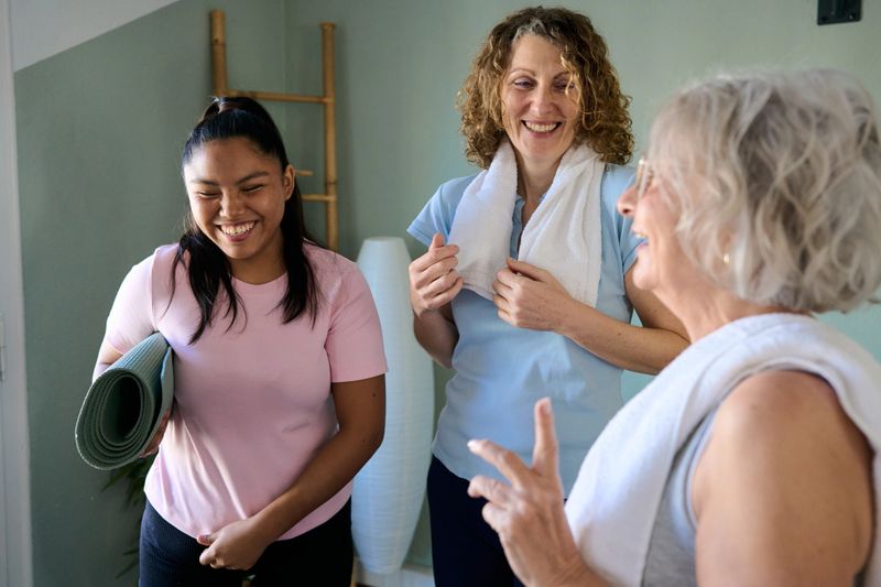 Diverse women laughing and talking together with yoga mats and towels after an exercise class, enjoying wellness