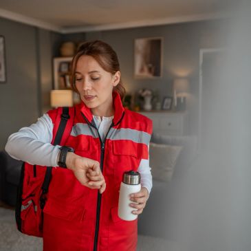 Woman in red vest checking her smartwatch and holding a water bottle.