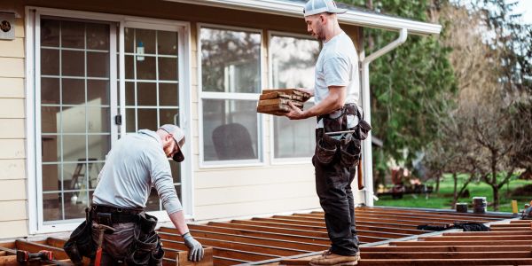 Two workers building a wooden deck outside a house.